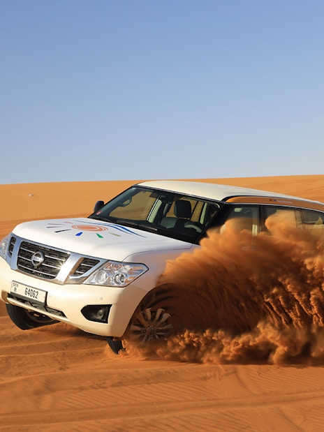 SUV driving through Arabian desert dunes on a safari tour.