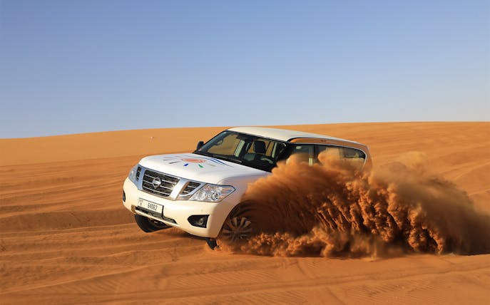 SUV driving through Arabian desert dunes on a safari tour.