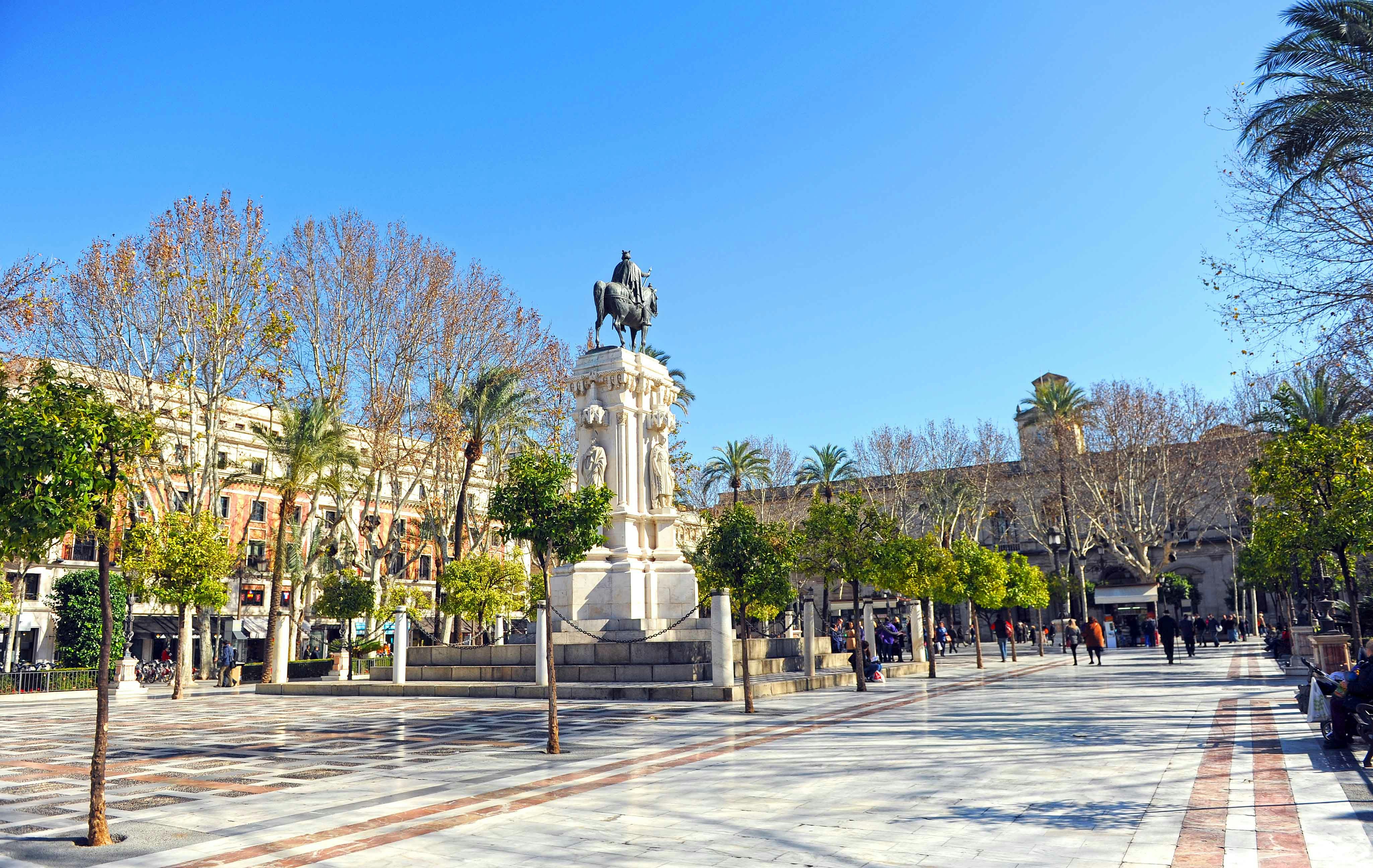 Equestrian statue in Plaza Nueva, Seville, surrounded by trees and historic buildings.