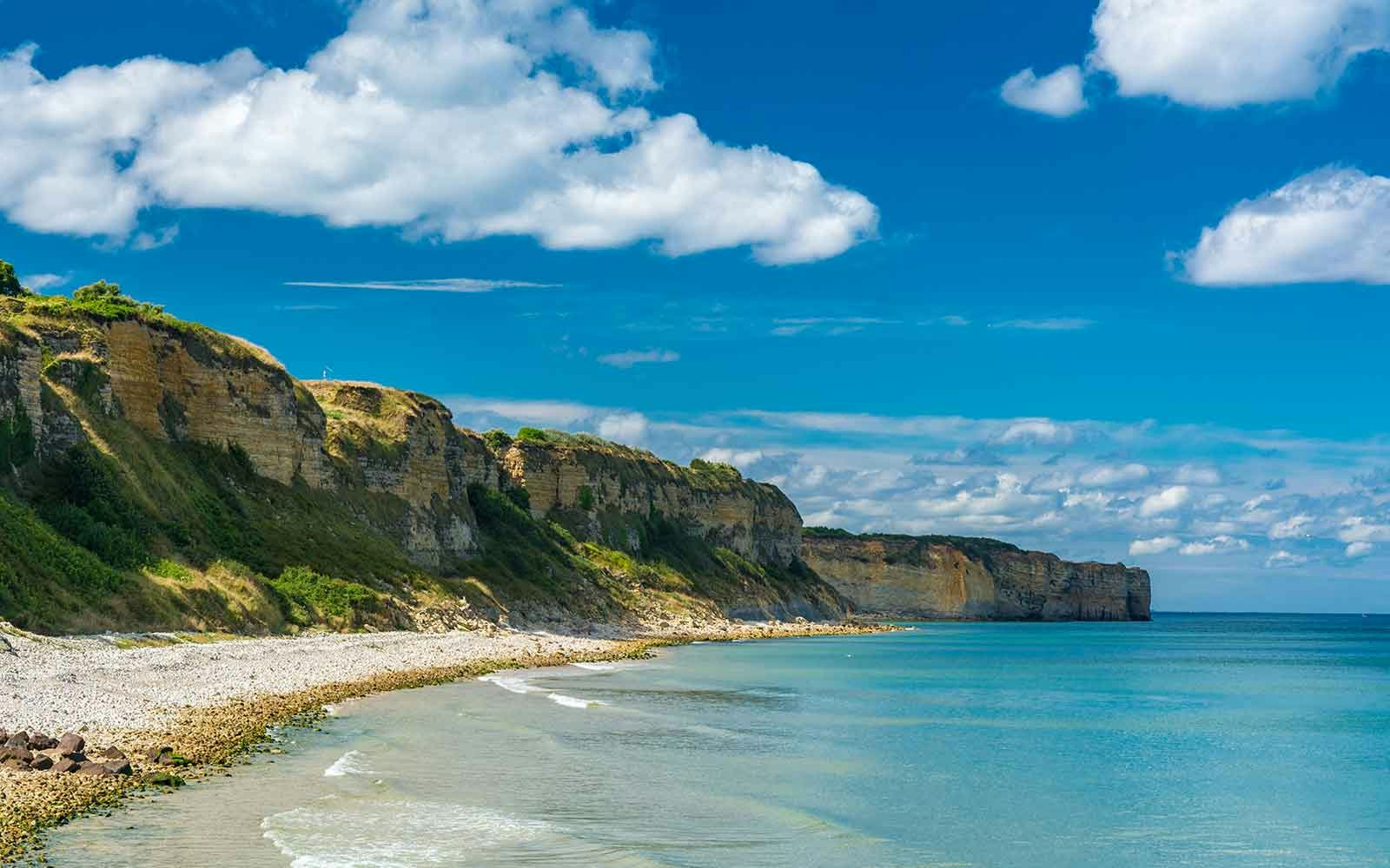 Visitors exploring Omaha Beach, Normandy, with historical World War II bunkers in the background.