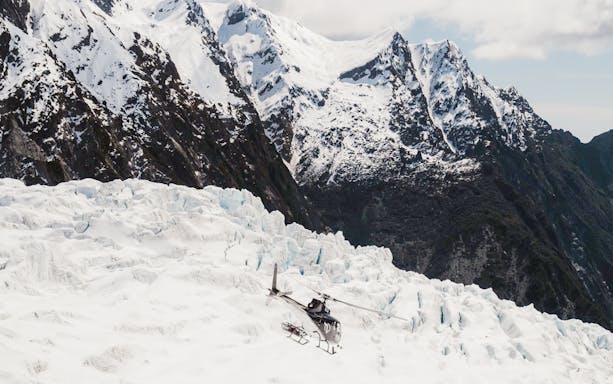 Helicopter flying over snowy mountain landscape with rugged peaks.