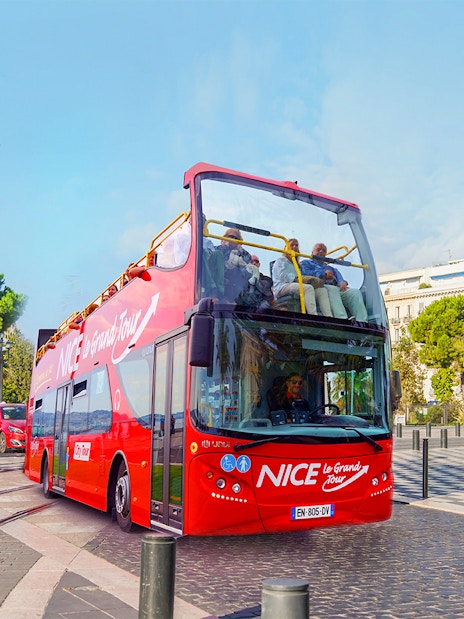 Open-top red tour bus in Nice, France, with passengers enjoying city views.