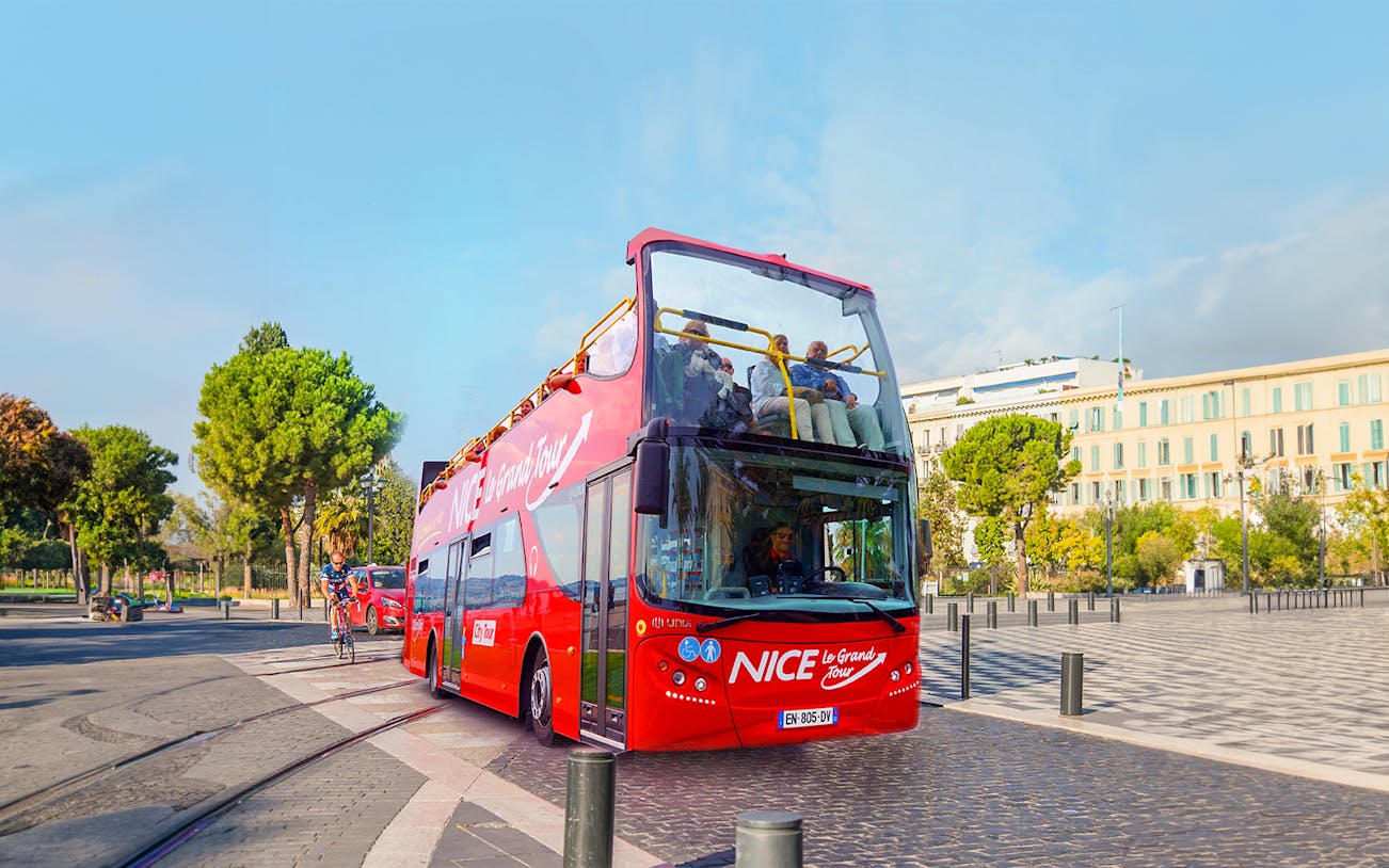 Open-top red tour bus in Nice, France, with passengers enjoying city views.