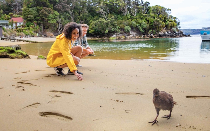 Couple interacting with a bird on a serene beach, surrounded by lush greenery.