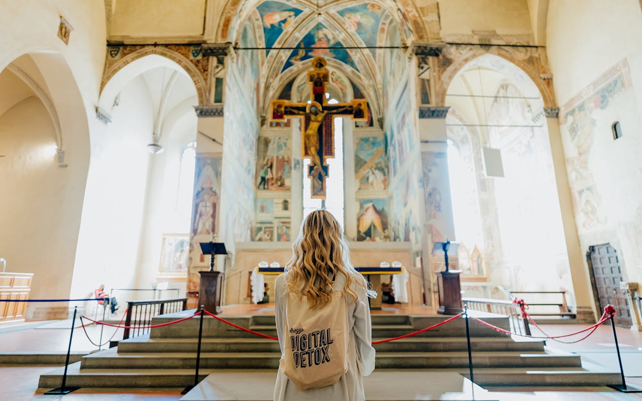 Visitor admiring frescoes and crucifix in Arezzo church during 2-hour smartphone-free tour.