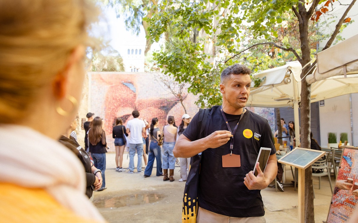 Tour guide leading a group in Barcelona near a mosaic wall.