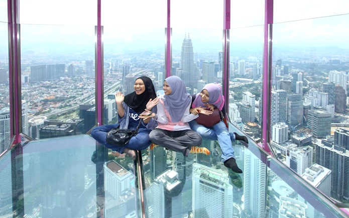 Female tourists sitting on KL Tower observation deck with city view.