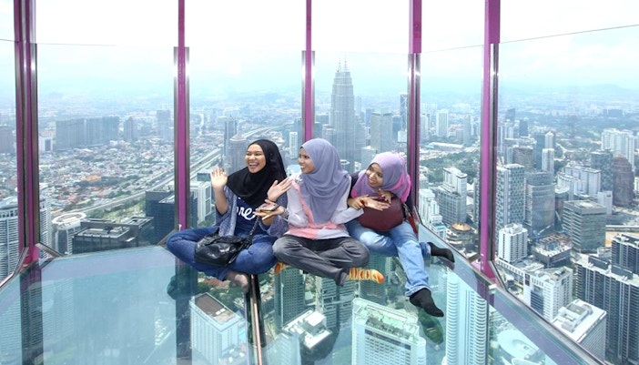 Female tourists sitting on KL Tower observation deck with city view.