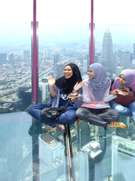 Female tourists sitting on KL Tower observation deck with city view.