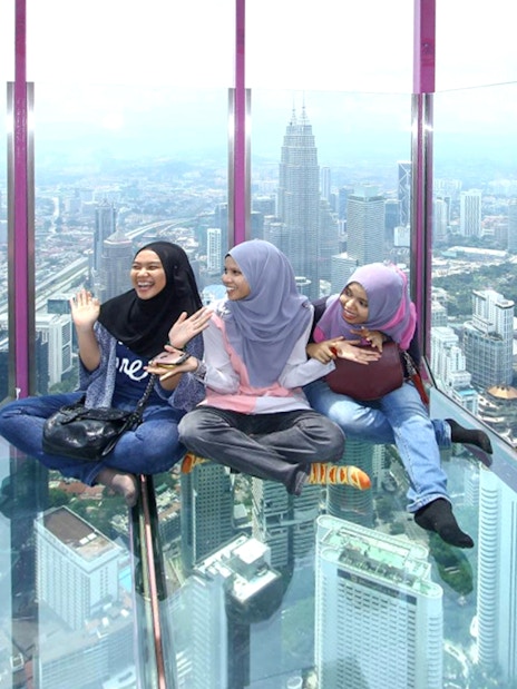 Female tourists sitting on KL Tower observation deck with city view.