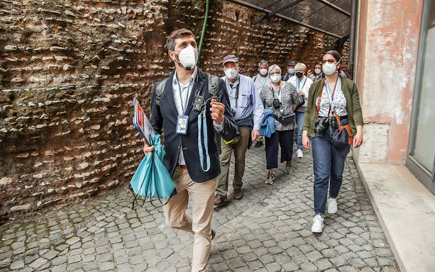 Tour group with guide at Castel Sant’Angelo, Rome, wearing masks and walking along ancient walls.