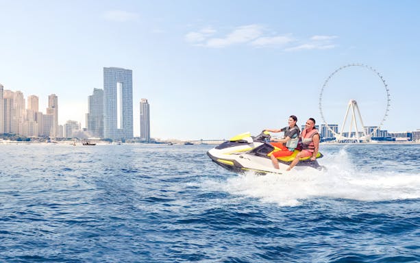 Jet ski riders near Burj Al Arab with Dubai skyline in background.