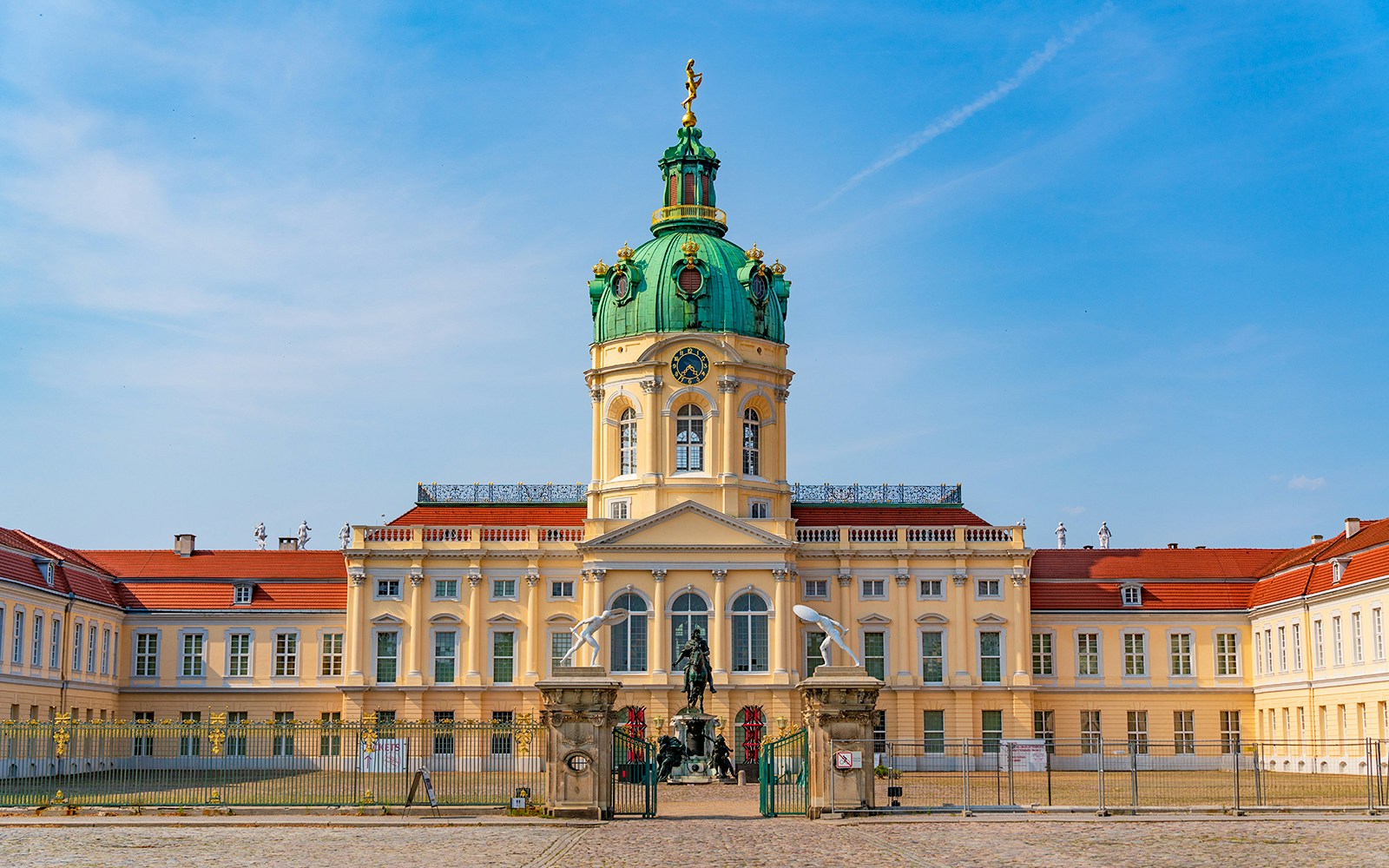 Schloss Charlottenburg in Berlin bei klarem Himmel, mit seiner grünen Kuppel und einer Statue am Eingang.