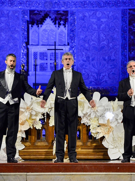 Opera singers performing on stage at a nighttime event with ornate blue backdrop.