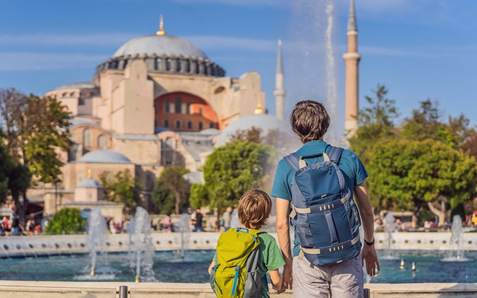 Visitors with backpacks view Hagia Sophia in Istanbul near a fountain.