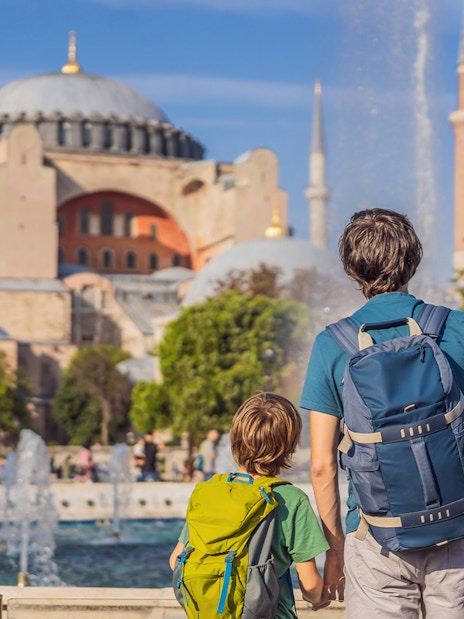 Visitors with backpacks view Hagia Sophia in Istanbul near a fountain.