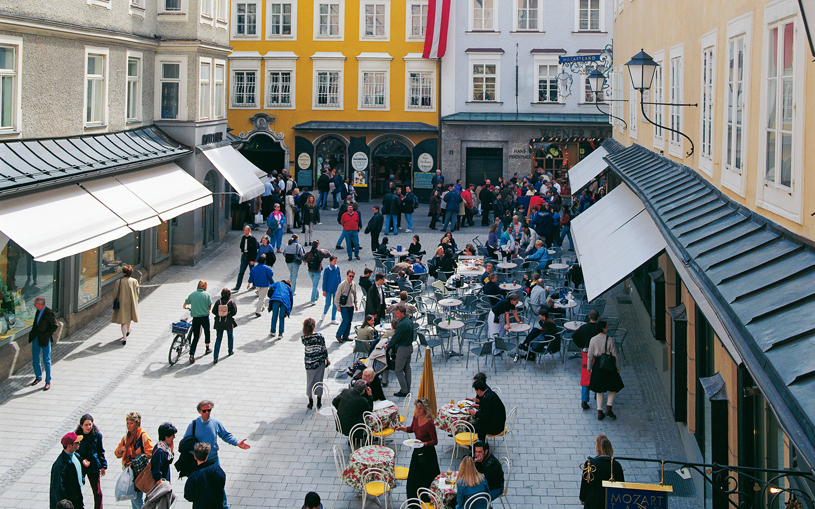 Crowded street with outdoor cafes and people in Salzburg on a Hop On Hop Off city tour.