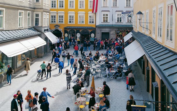 Crowded street with outdoor cafes and people in Salzburg on a Hop On Hop Off city tour.