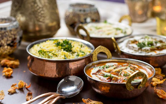 Traditional Indian dishes in copper bowls with rice and curry, garnished with herbs.