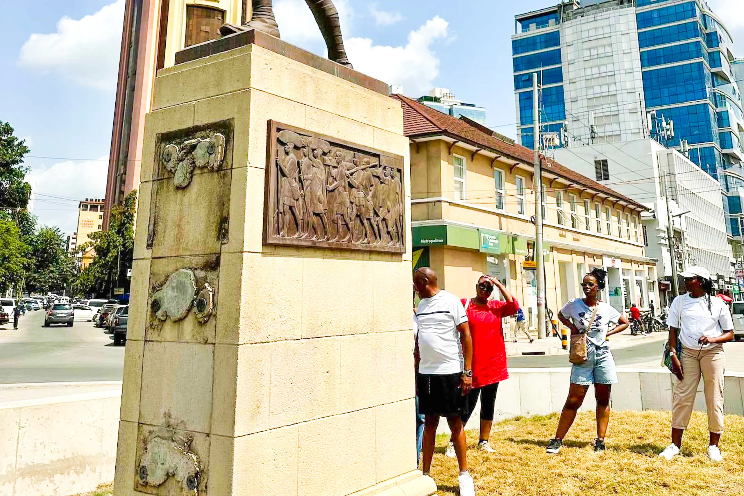 Monument with historical relief in Dar es Salaam city center, tourists exploring nearby.