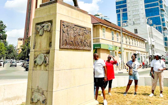 Monument with historical relief in Dar es Salaam city center, tourists exploring nearby.