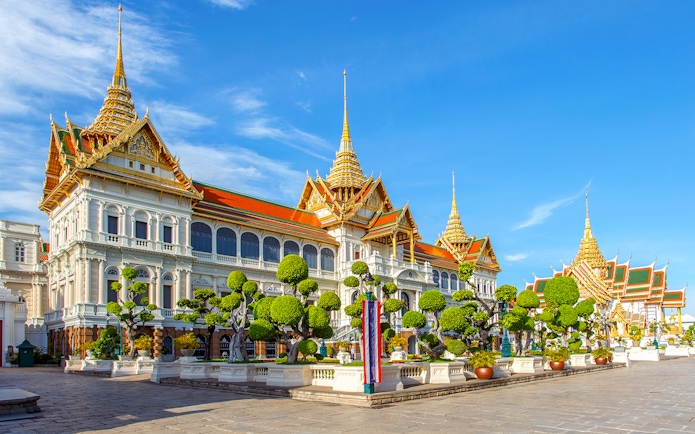 Grand Palace in Bangkok with ornate architecture and manicured gardens.