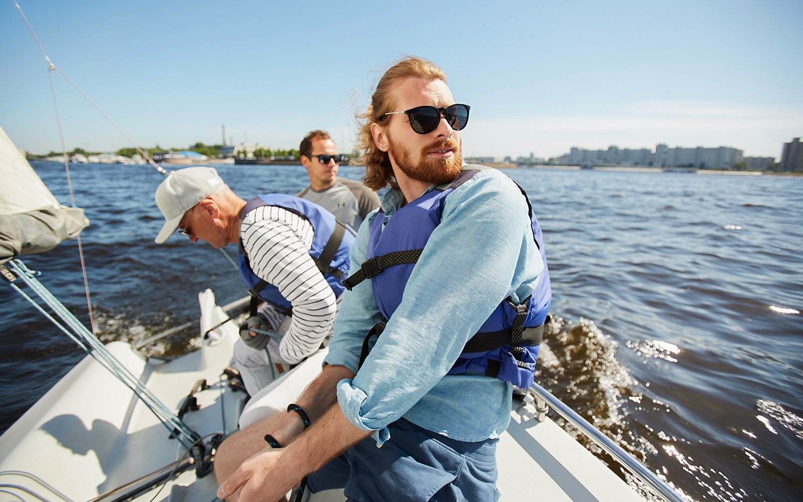 Tourists wearing life jackets, enjoying a yacht trip with friends on a sunny day