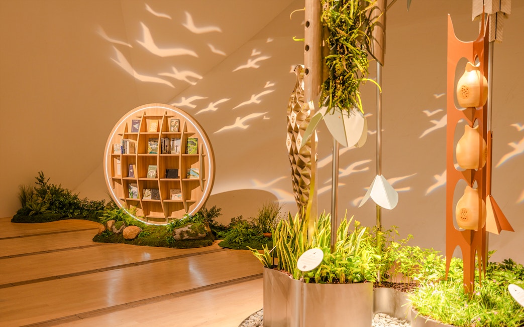 Circular bookshelf with books and plants in a well-lit exhibit space, bird silhouettes projected on walls.