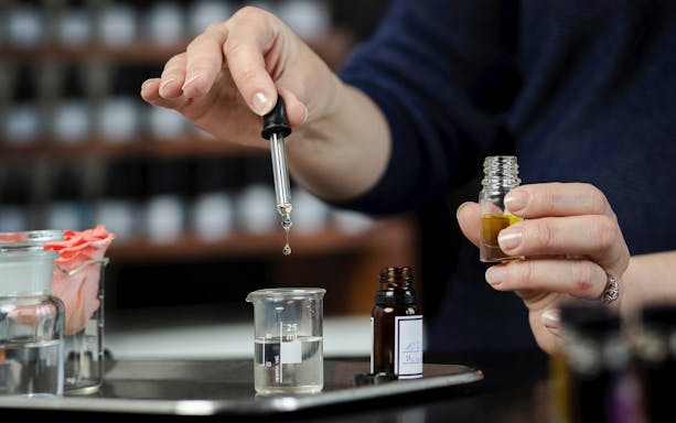 Mixing fragrances with a dropper into a small bottle.
