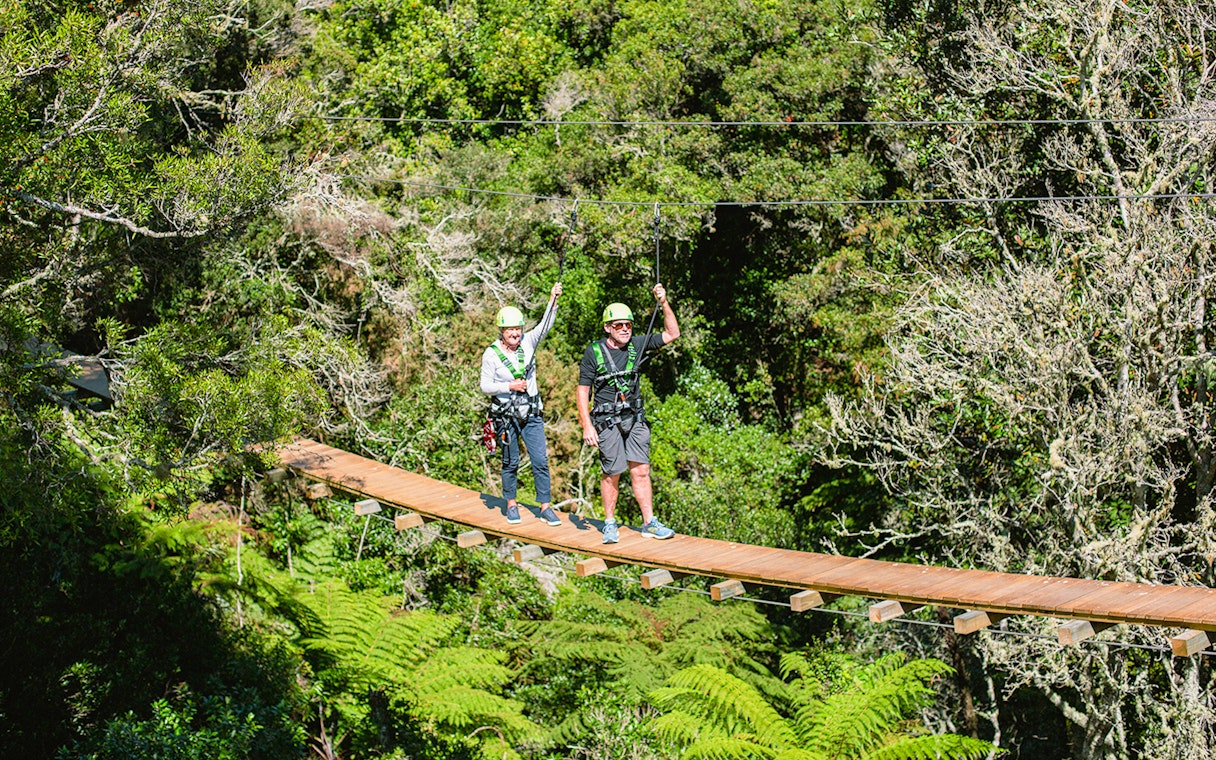 Two people crossing a suspension bridge in Rotorua forest during a zipline tour.