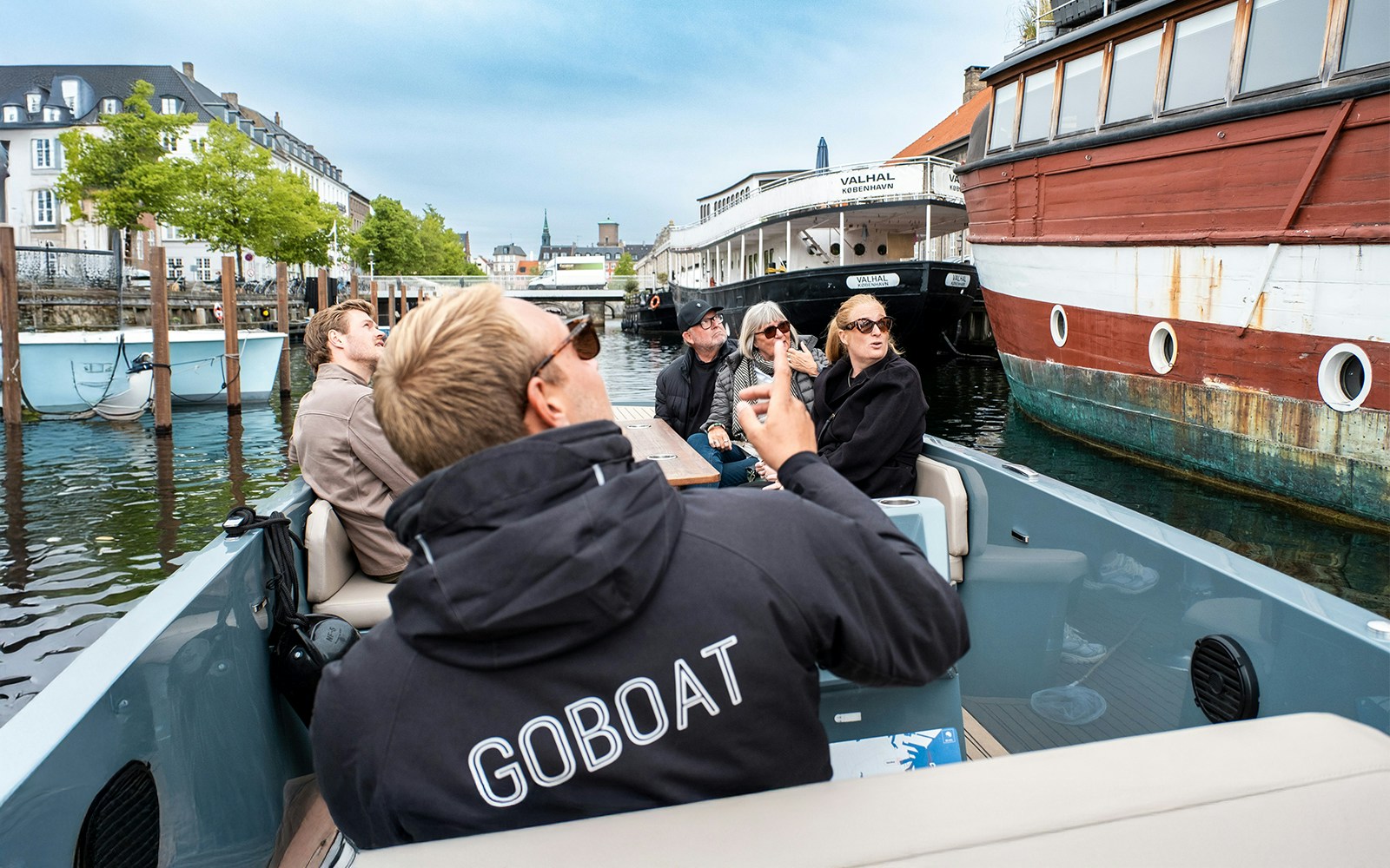 Guests on electric boat tour in Copenhagen, captain pedaling through city canals.