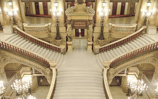 Grand staircase inside Opéra Garnier, Paris, with ornate chandeliers and sculptures.