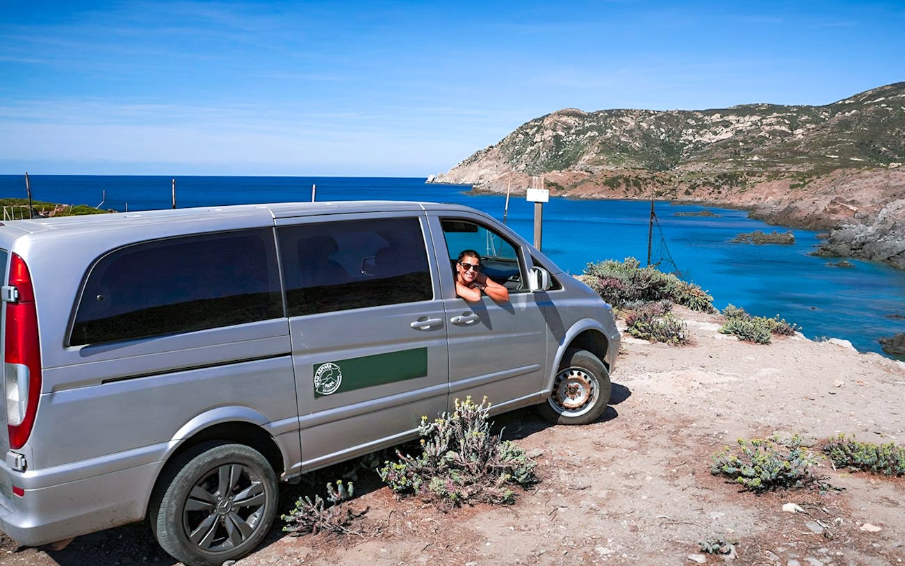 Van parked by the coast with a person enjoying the view at Asinara National Park.