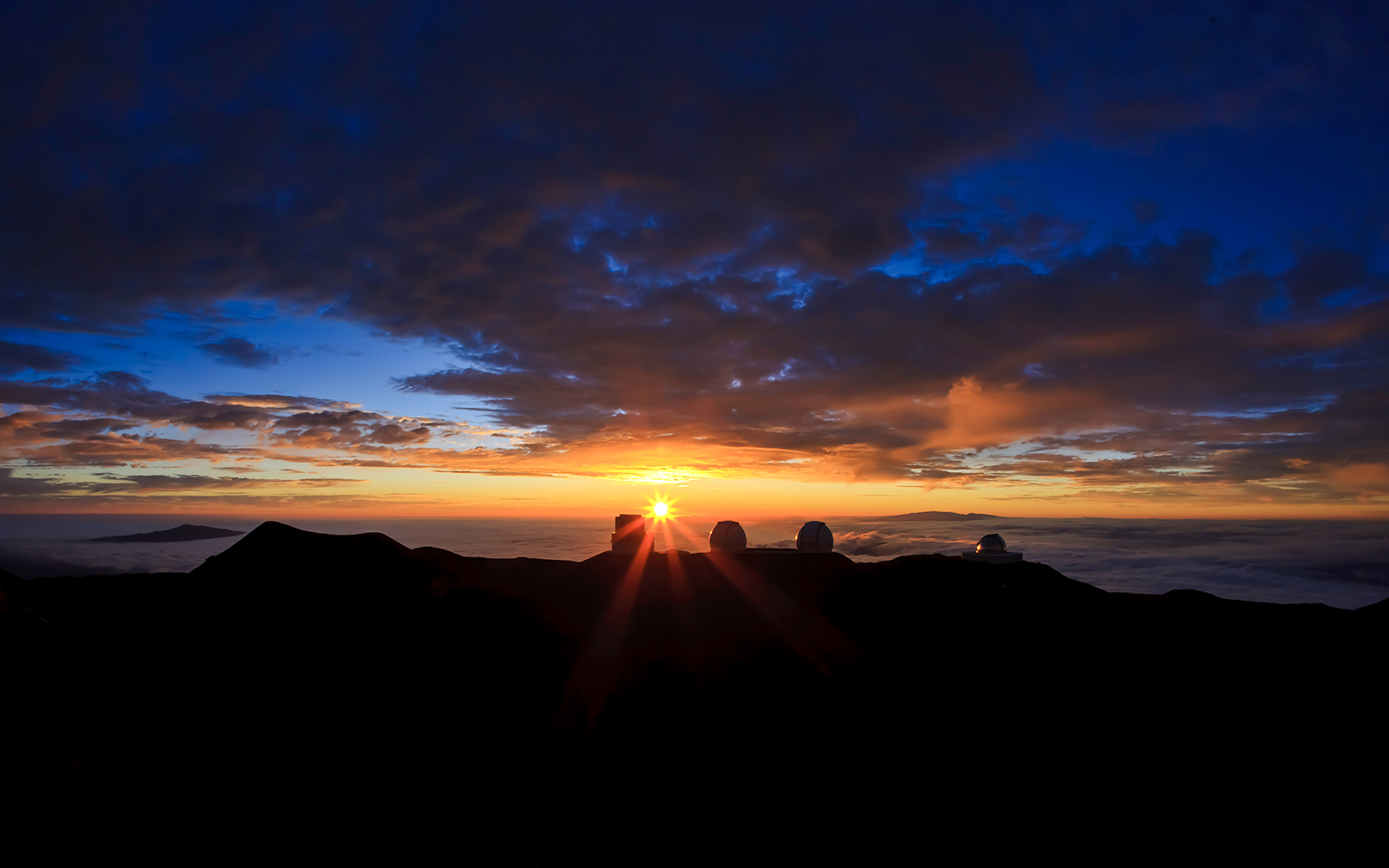 Mauna Kea Observatory domes silhouetted against a vibrant sunset sky.