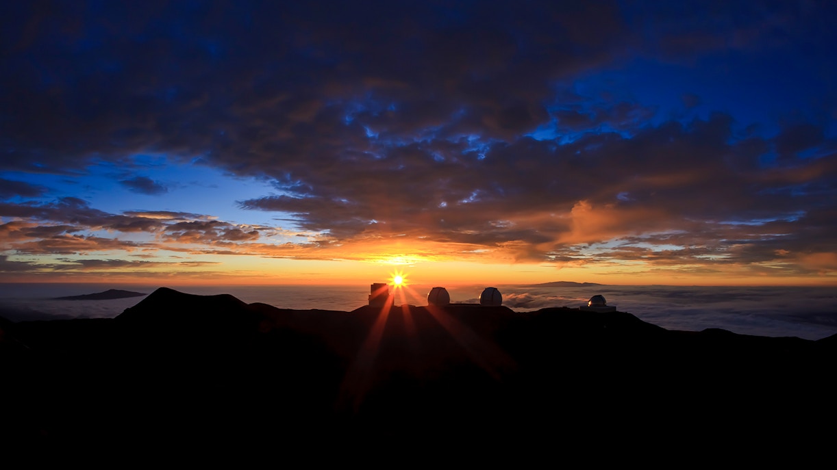 Mauna Kea Observatory domes silhouetted against a vibrant sunset sky.