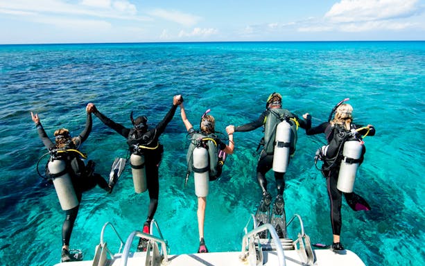 Scuba divers jumping off boat into clear ocean on full-day tour.
