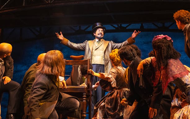 Performer in top hat engaging audience during Sweeney Todd musical scene.
