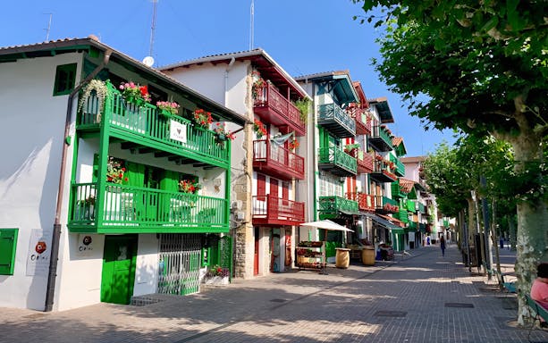 Colorful buildings with balconies in Hondarribia, Spain, on a sunny street lined with trees.