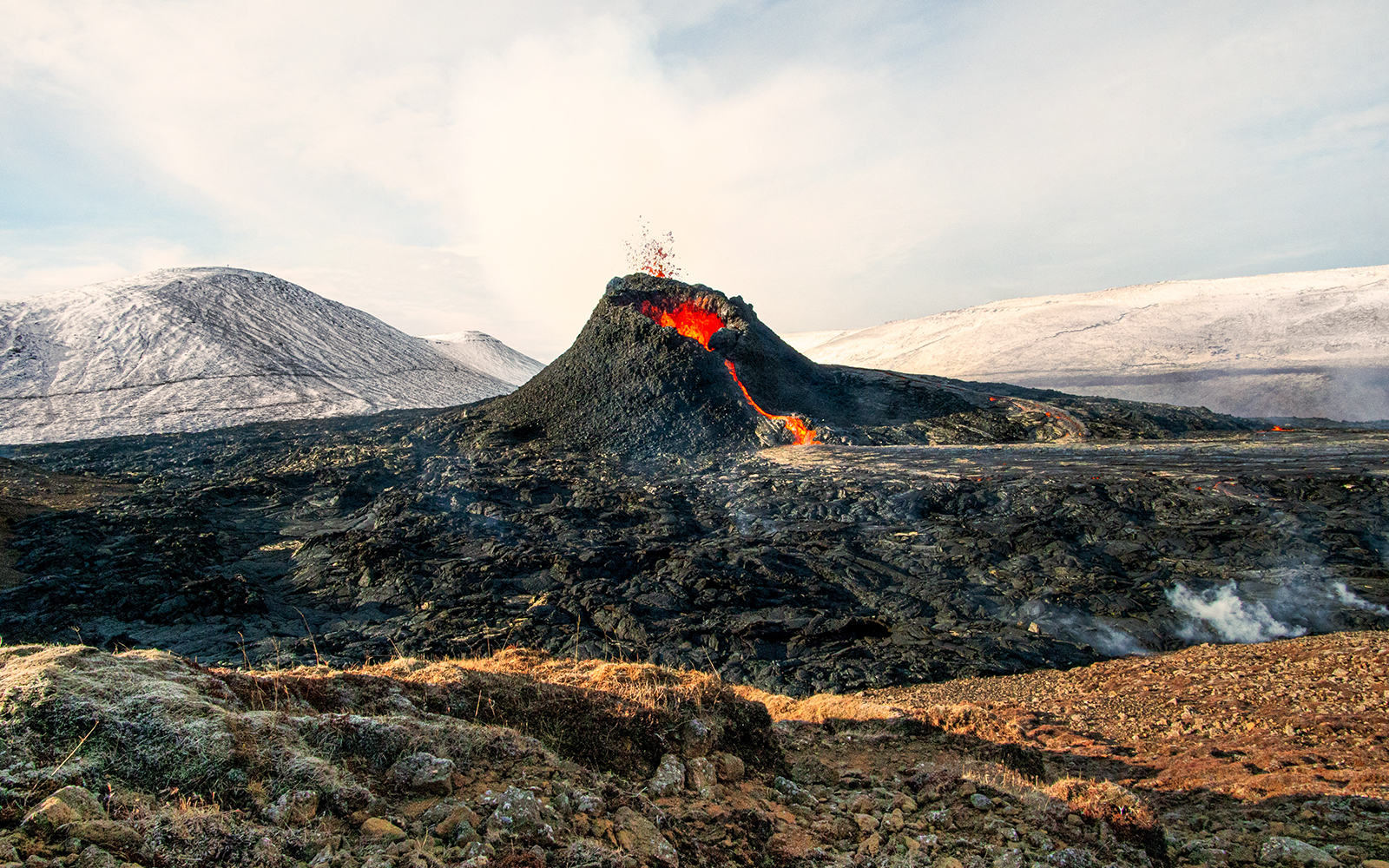 Volcano erupting with lava flow in Icelandic landscape.