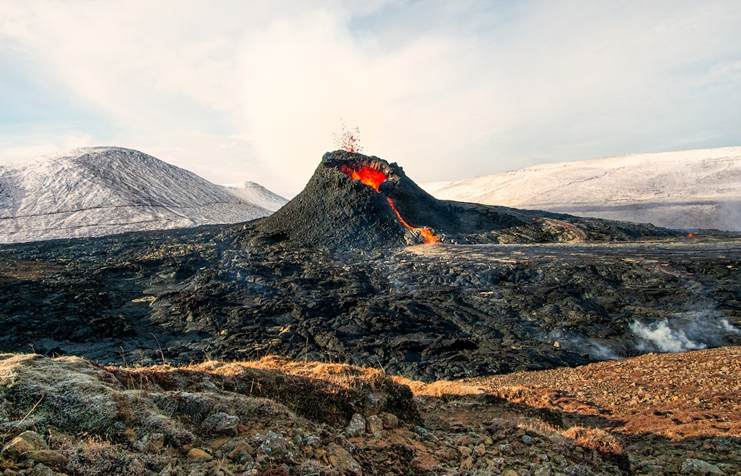 Volcano erupting with lava flow in Icelandic landscape.