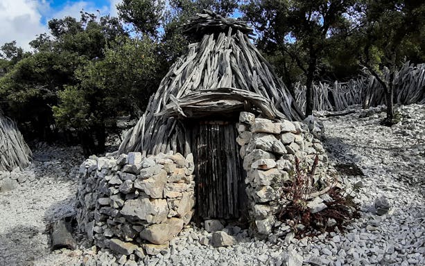 Stone and wood hut along the trekking path in Cala Mariolu, surrounded by trees.