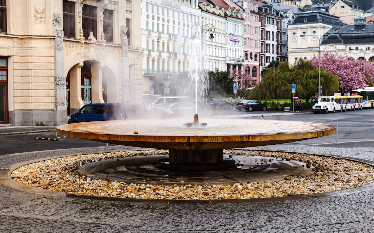 Geyser of mineral water in Karlovy Vary with historic buildings in the background.