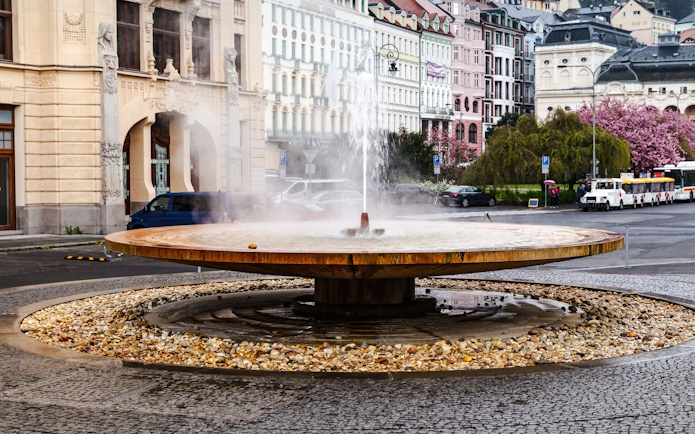 Geyser of mineral water in Karlovy Vary with historic buildings in the background.