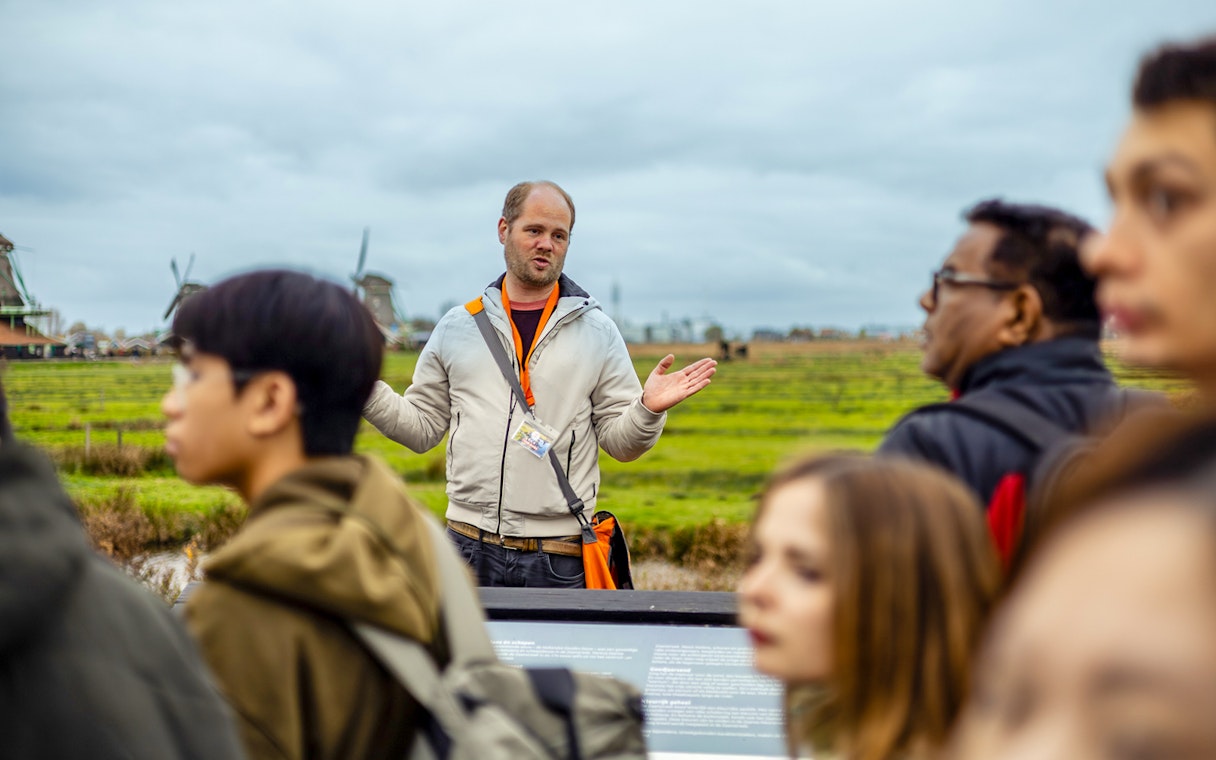 Guide explaining Zaanse Schans windmills to tourists on Keukenhof tour.