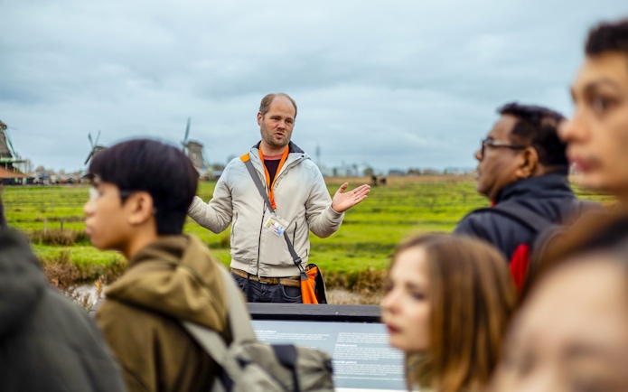 Guide explaining Zaanse Schans windmills to tourists on Keukenhof tour.