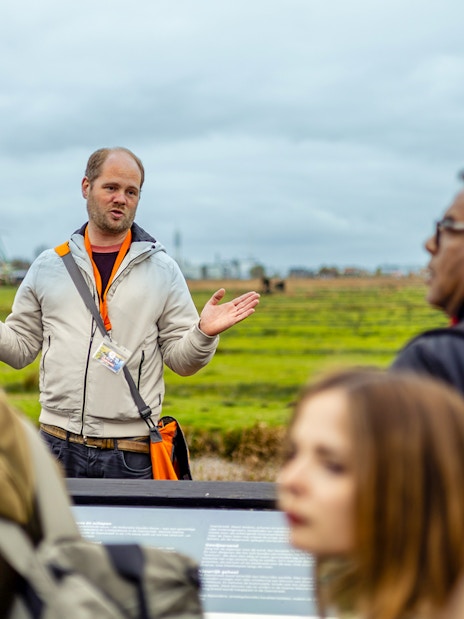 Guide explaining Zaanse Schans windmills to tourists on Keukenhof tour.