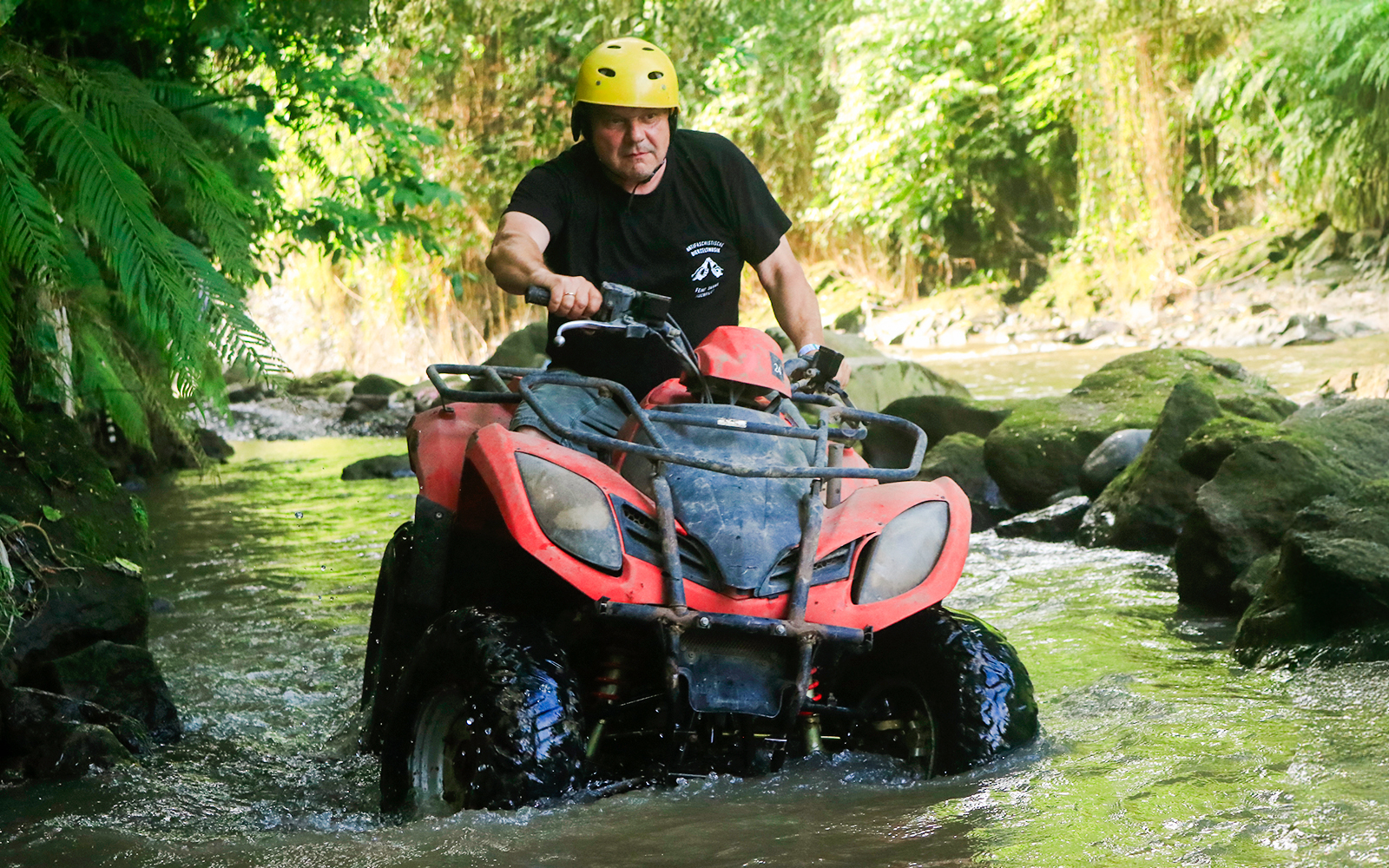 ATV navigating a rocky stream in Bali jungle.