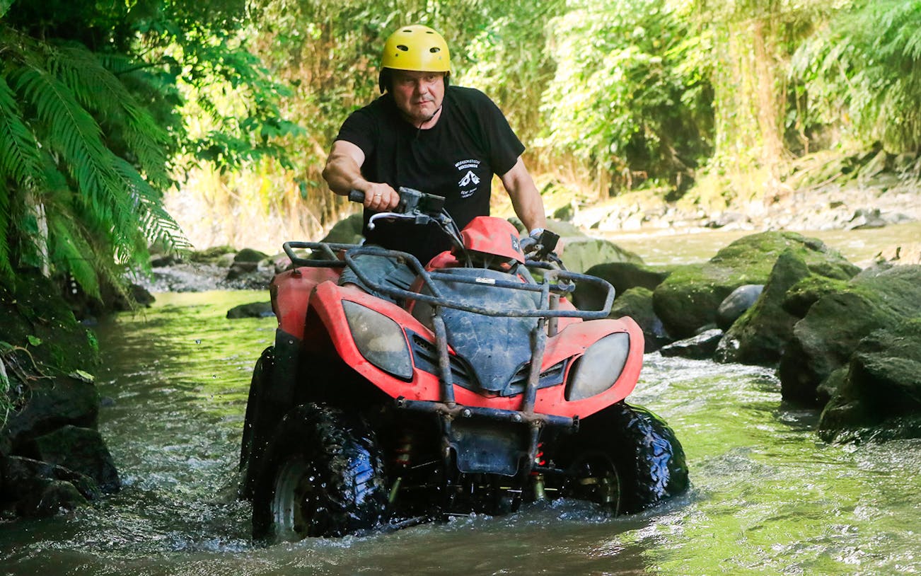 ATV navigating a rocky stream in Bali jungle.