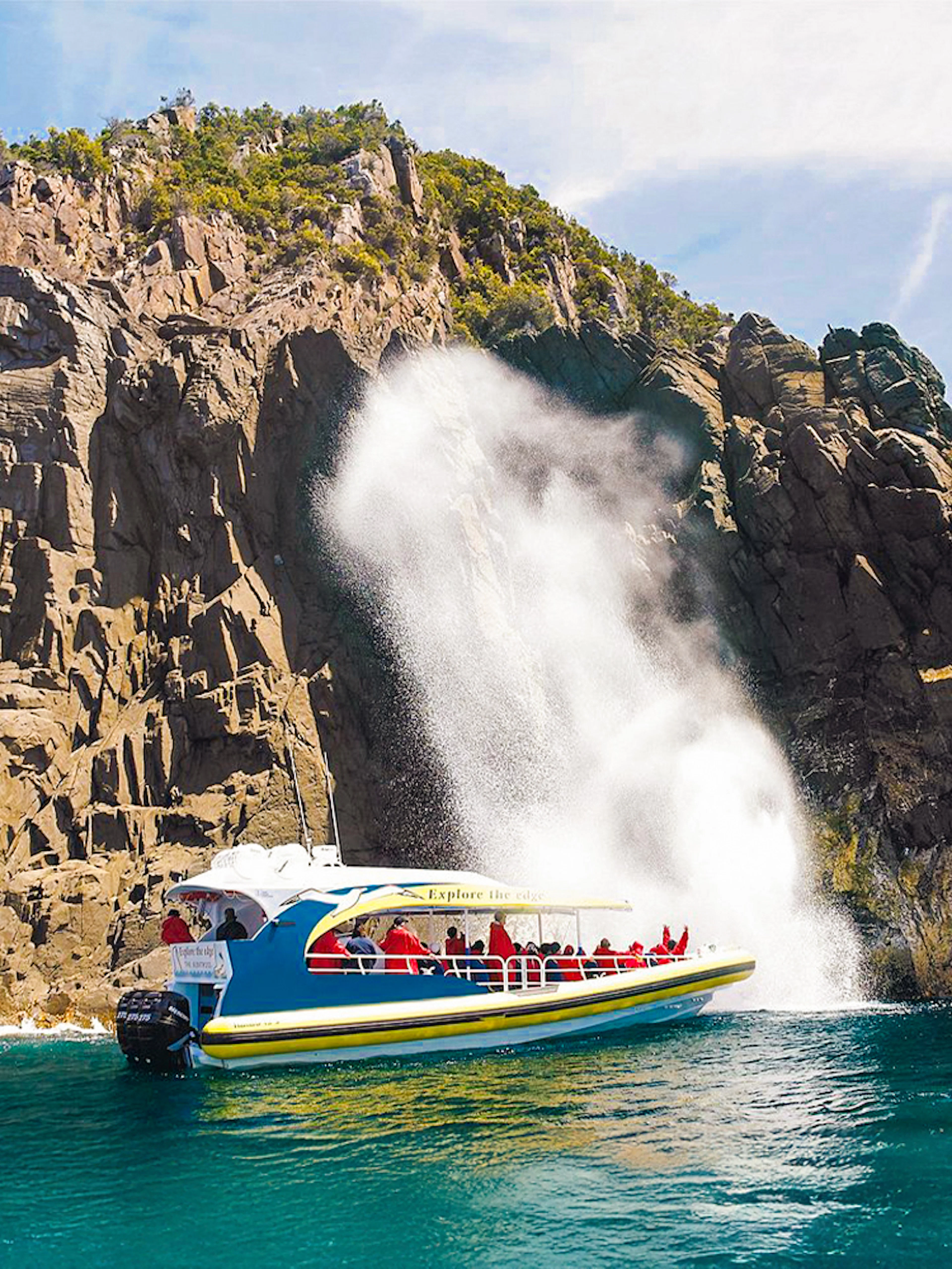 Cruise boat near rocky cliffs and waterfall on Bruny Island Wilderness Cruise.