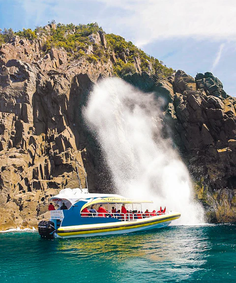 Cruise boat near rocky cliffs and waterfall on Bruny Island Wilderness Cruise.